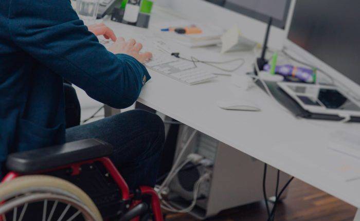 Disabled man at work in a wheelchair sitting at a desk using a computer