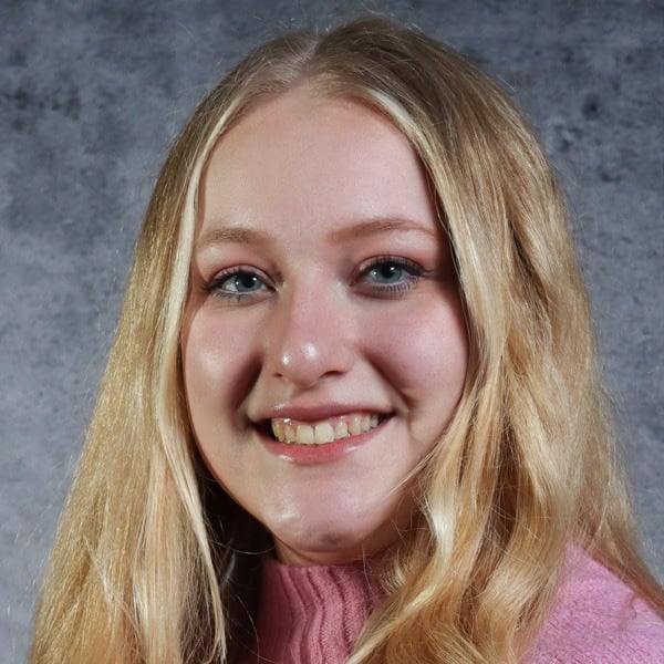 Smiling person in pink sweater against gray background.