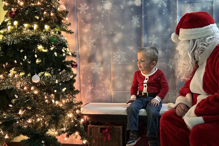 Child with Santa by Christmas tree indoors.